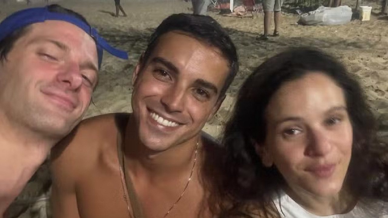 rês pessoas tiram selfie na areia de Ipanema durante a noite.